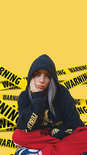 Billie Eilish in Black Hoodie Against Yellow Warning Tape Background HD phone wallpaper