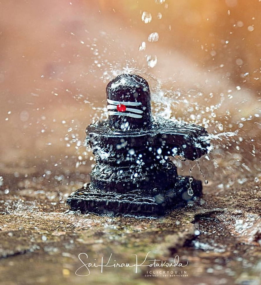 Black Shivling with Water Splash and White Ticks on Warm Background HD phone wallpaper