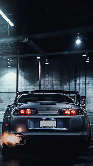 Rear View of a Modified Toyota Supra MK4 with Exhaust Flame in a Dark Garage HD phone wallpaper