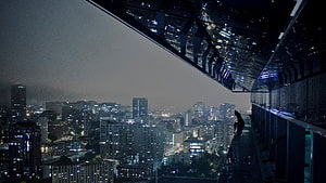Silhouette of a Person Sitting on a High-Rise Balcony Overlooking a Rainy City at Night HD wallpaper