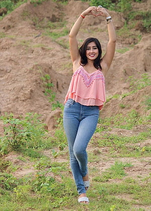 Sofia Ansari posing outdoors in a pink top and blue jeans with hands forming a heart shape HD phone wallpaper