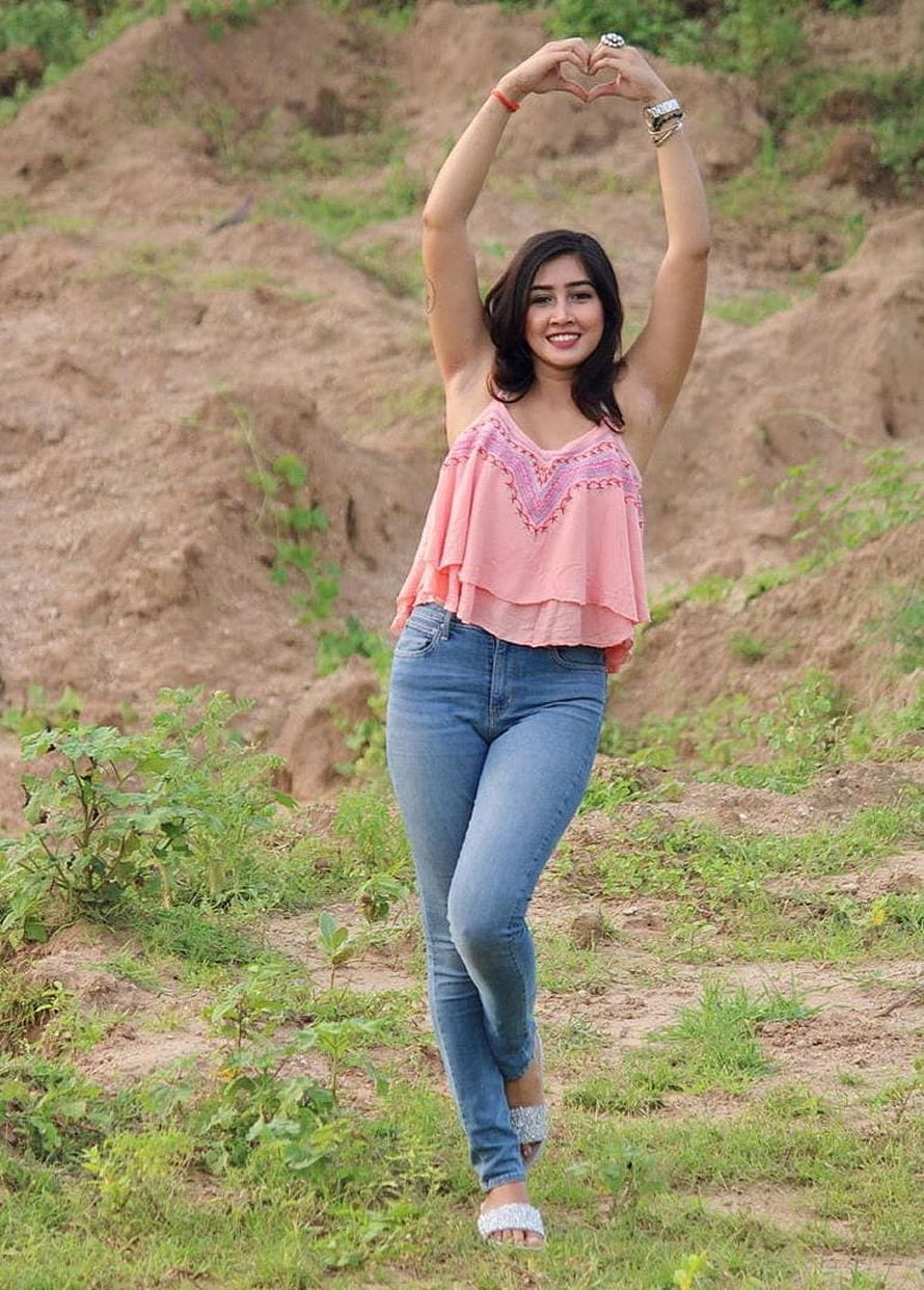 Sofia Ansari posing outdoors in a pink top and blue jeans with hands forming a heart shape HD phone wallpaper