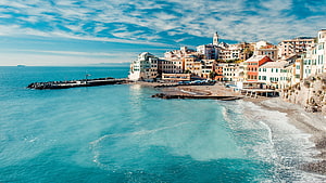 Colorful Mediterranean coastal town with turquoise sea and pebble beach under a bright blue sky HD wallpaper