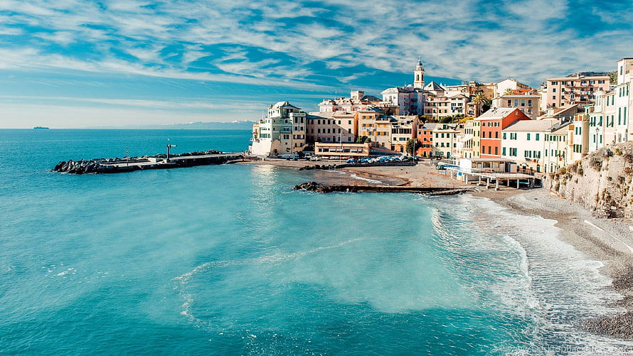 Colorful Mediterranean coastal town with turquoise sea and pebble beach under a bright blue sky HD wallpaper