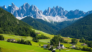 Alpine Village with Church Nestled in Green Meadows Beneath Dramatic Dolomite Peaks HD wallpaper