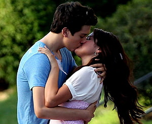 Young couple sharing a passionate kiss in a lush green outdoor setting HD wallpaper