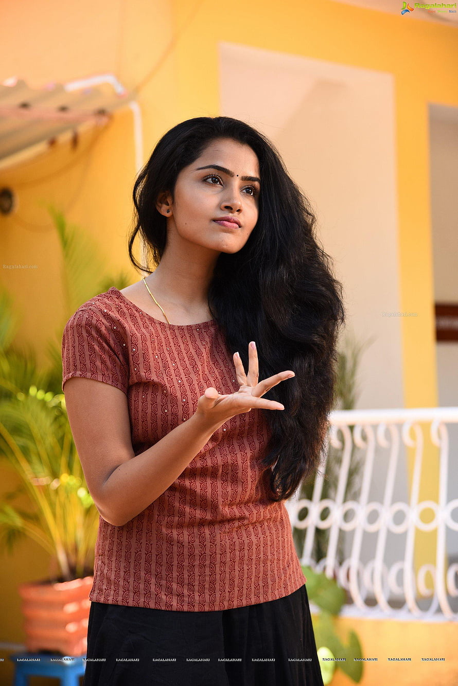 Anupama Parameswaran in a rust patterned top with long dark hair against a warm yellow wall HD phone wallpaper