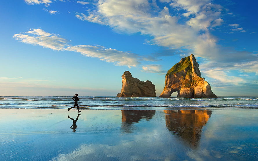 Woman Jogging on Wet Sand with Dramatic Sea Stacks and Reflections HD wallpaper
