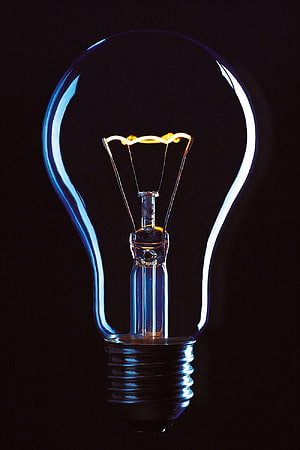 Glowing Incandescent Light Bulb with Visible Filament on Black Background HD phone wallpaper