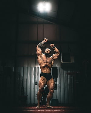 Muscular Bodybuilder Striking a Victory Pose in a Dark Industrial Gym HD phone wallpaper