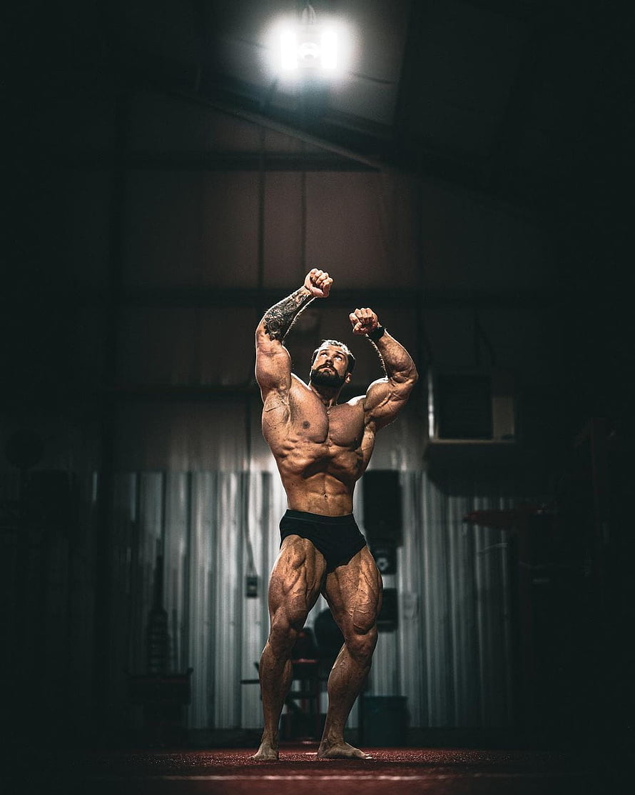 Muscular Bodybuilder Striking a Victory Pose in a Dark Industrial Gym HD phone wallpaper