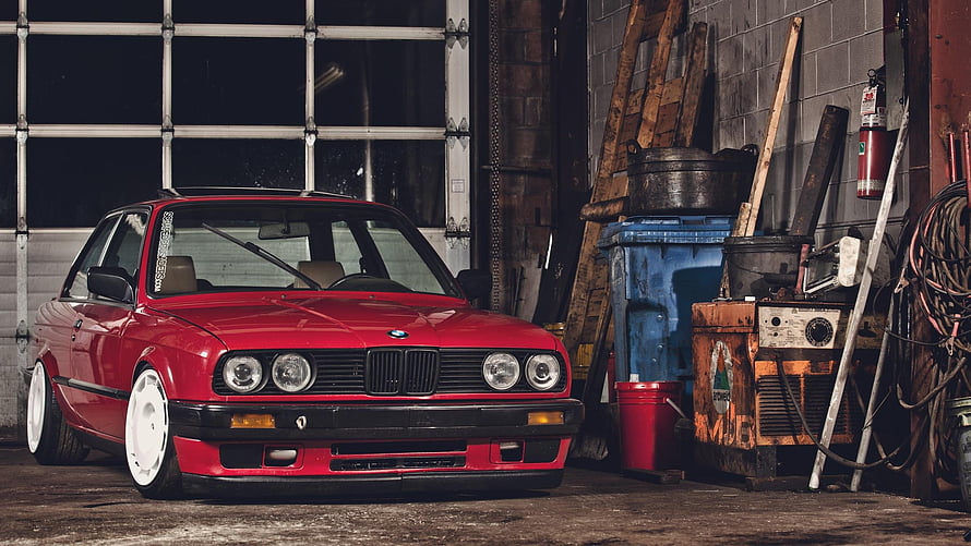 Red BMW E30 Coupe with White Wheels Parked in a Cluttered Garage Workshop HD wallpaper