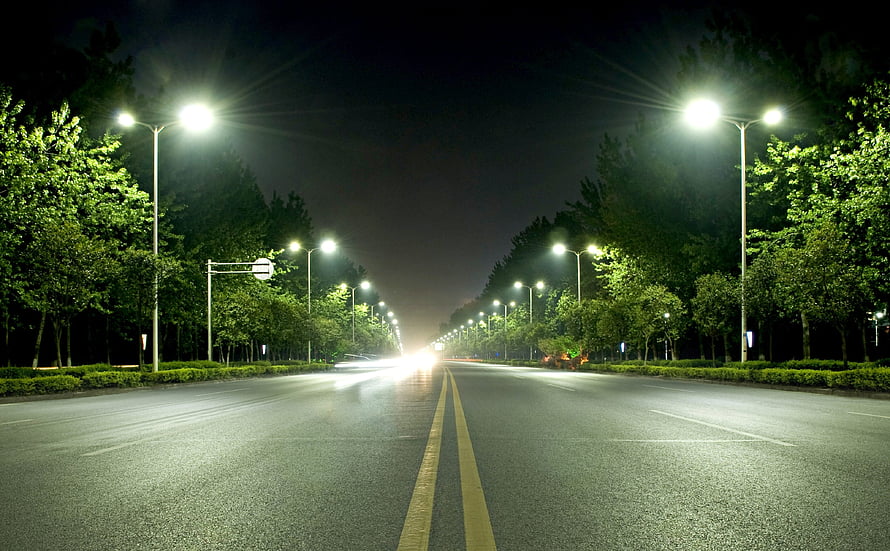 Empty City Boulevard at Night with Glowing Streetlights and Lush Green Trees HD wallpaper