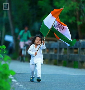 Young child in white kurta walking on a path while holding a large Indian national flag HD phone wallpaper