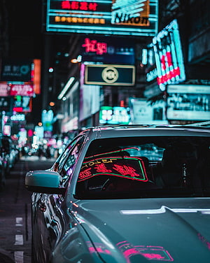 Neon-lit Tokyo street at night with a sleek car reflecting vibrant city signage HD phone wallpaper
