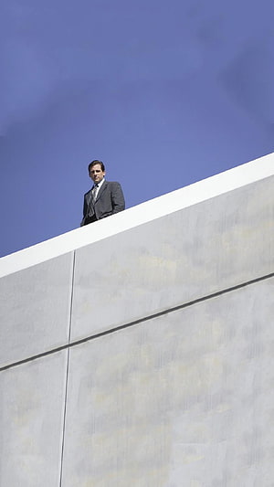 Michael Scott standing on a modern concrete building ledge against a clear blue sky HD phone wallpaper