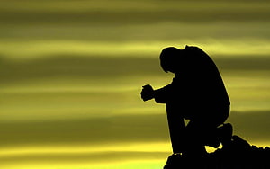 Silhouette of a man kneeling in contemplation against a golden sunset sky HD wallpaper