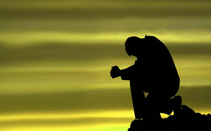 Silhouette of a man kneeling in contemplation against a golden sunset sky HD wallpaper