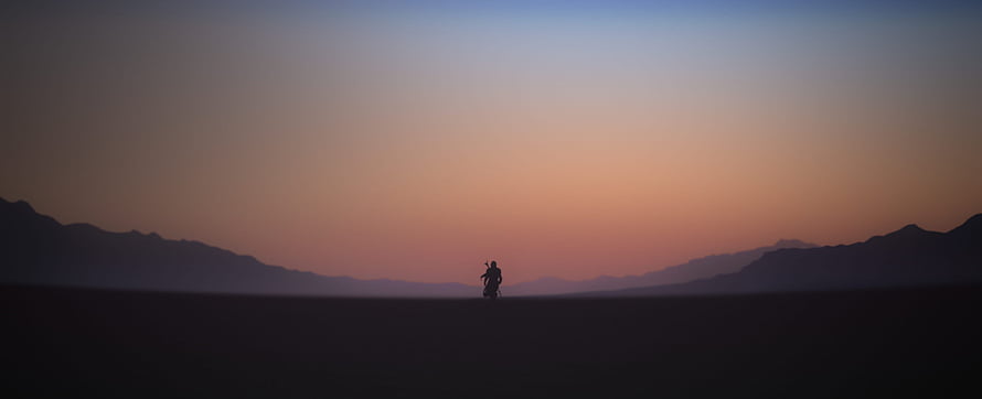 The Mandalorian Silhouette Riding Through Vast Desert at Sunset HD wallpaper