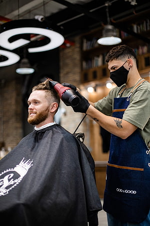 Barber Styling a Bearded Man's Hair with a Blow Dryer in a Modern Barbershop HD phone wallpaper
