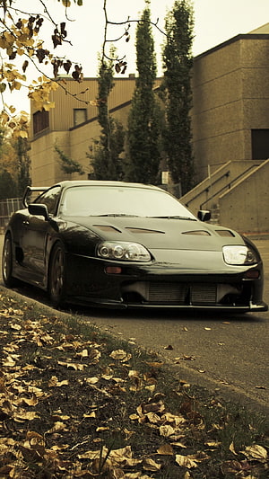 Black Toyota Supra MK4 parked on an autumn street with fallen leaves and industrial buildings in the background HD phone wallpaper