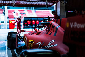 Ferrari Formula 1 car in the pit garage with crew members and track in the background HD wallpaper