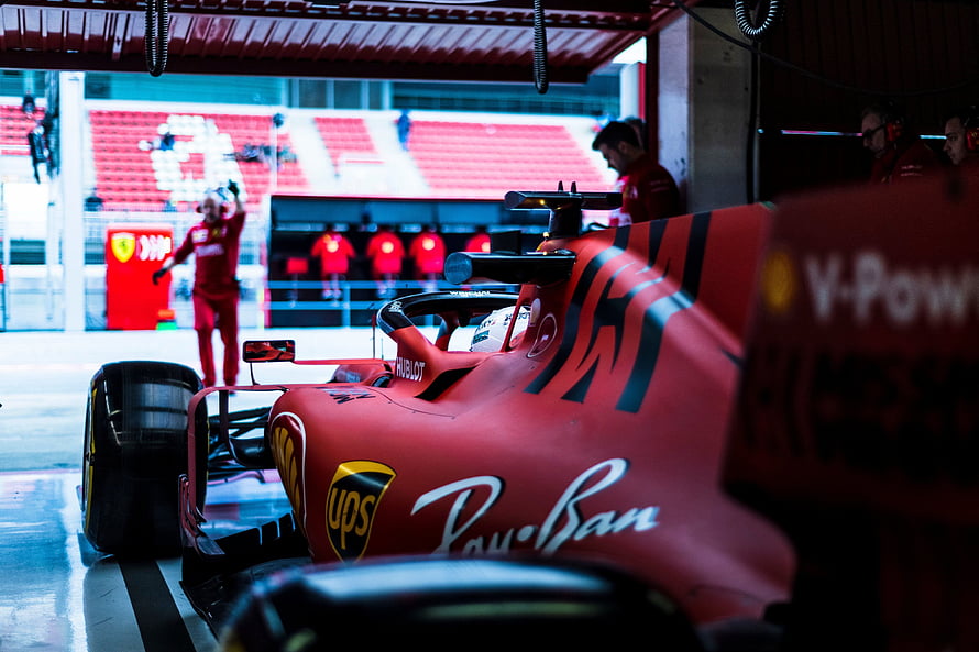 Ferrari Formula 1 car in the pit garage with crew members and track in the background HD wallpaper