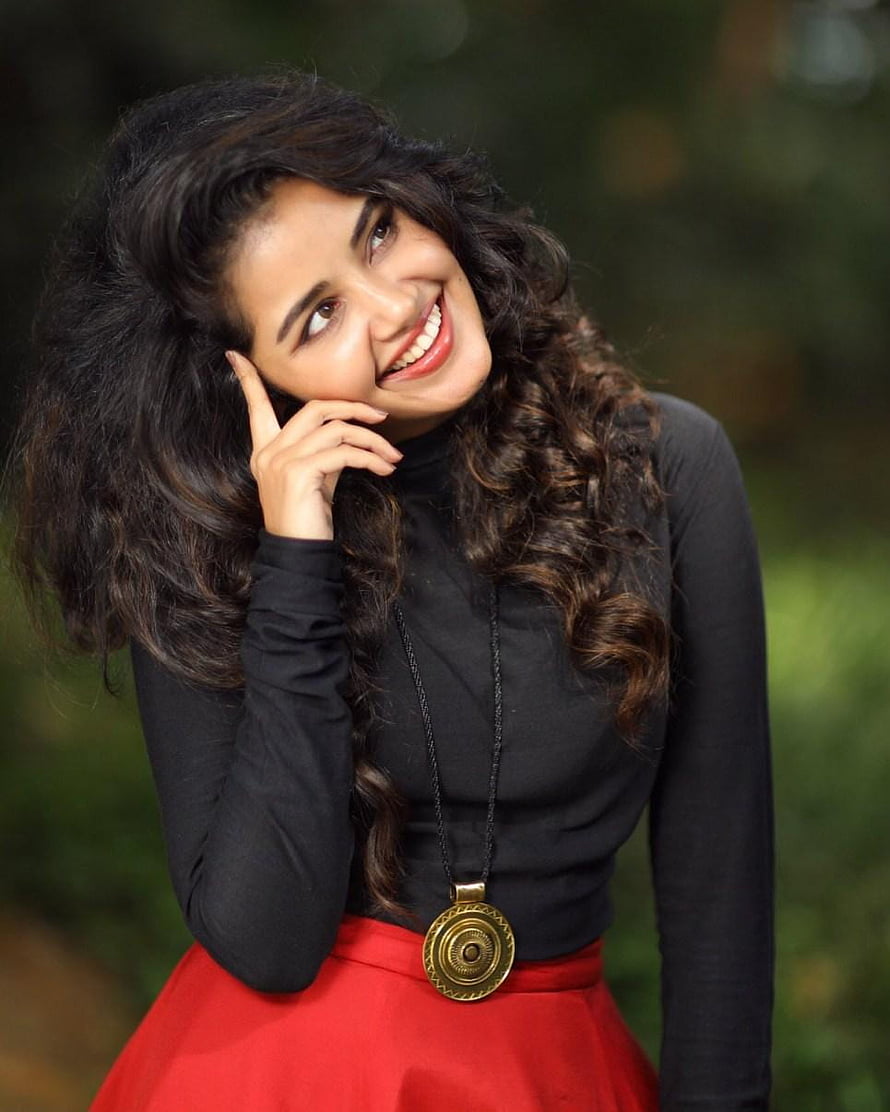 Anupama Parameswaran smiling portrait in black turtleneck and red skirt with gold pendant necklace HD phone wallpaper