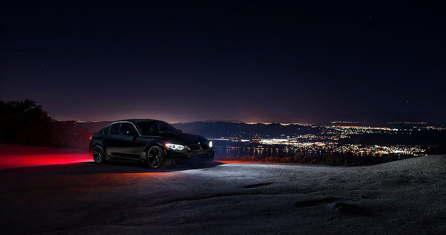 Black BMW M4 Sedan Parked on Hilltop Overlooking City Lights at Night HD wallpaper