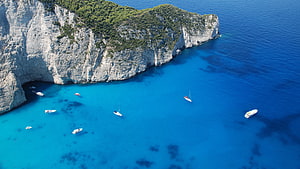 Aerial View of Turquoise Coves and White Sailboats Along Dramatic Coastal Cliffs HD wallpaper