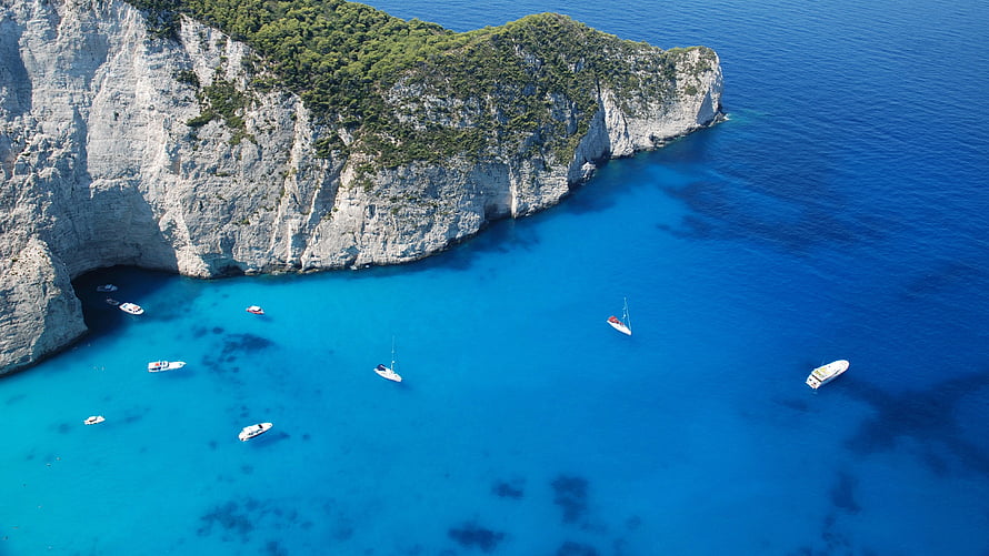 Aerial View of Turquoise Coves and White Sailboats Along Dramatic Coastal Cliffs HD wallpaper