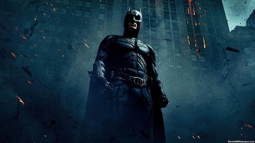 Batman in armored suit standing in smoky urban ruins with sparks and debris HD wallpaper