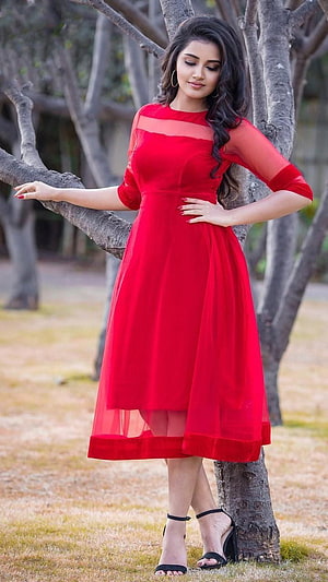 Anupama Parameswaran in a flowing red chiffon dress posing outdoors by a tree HD phone wallpaper