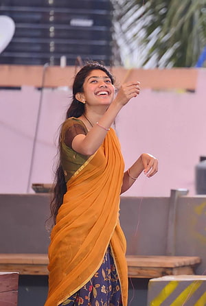 Sai Pallavi in a vibrant orange saree with a green blouse, smiling joyfully outdoors HD phone wallpaper