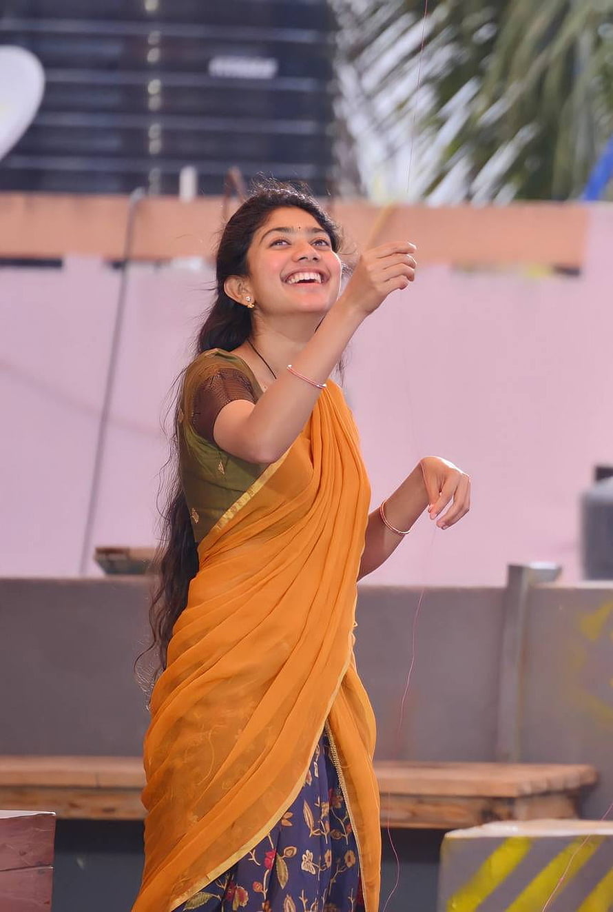 Sai Pallavi in a vibrant orange saree with a green blouse, smiling joyfully outdoors HD phone wallpaper