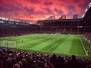 Old Trafford Stadium at Dusk with Dramatic Red Sky Over the Pitch HD wallpaper