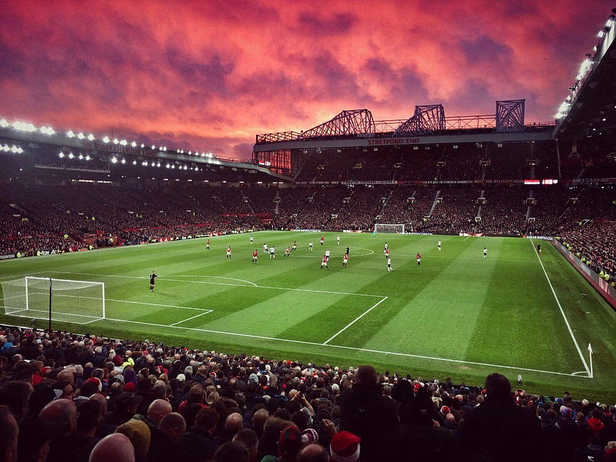Old Trafford Stadium at Dusk with Dramatic Red Sky Over the Pitch HD wallpaper