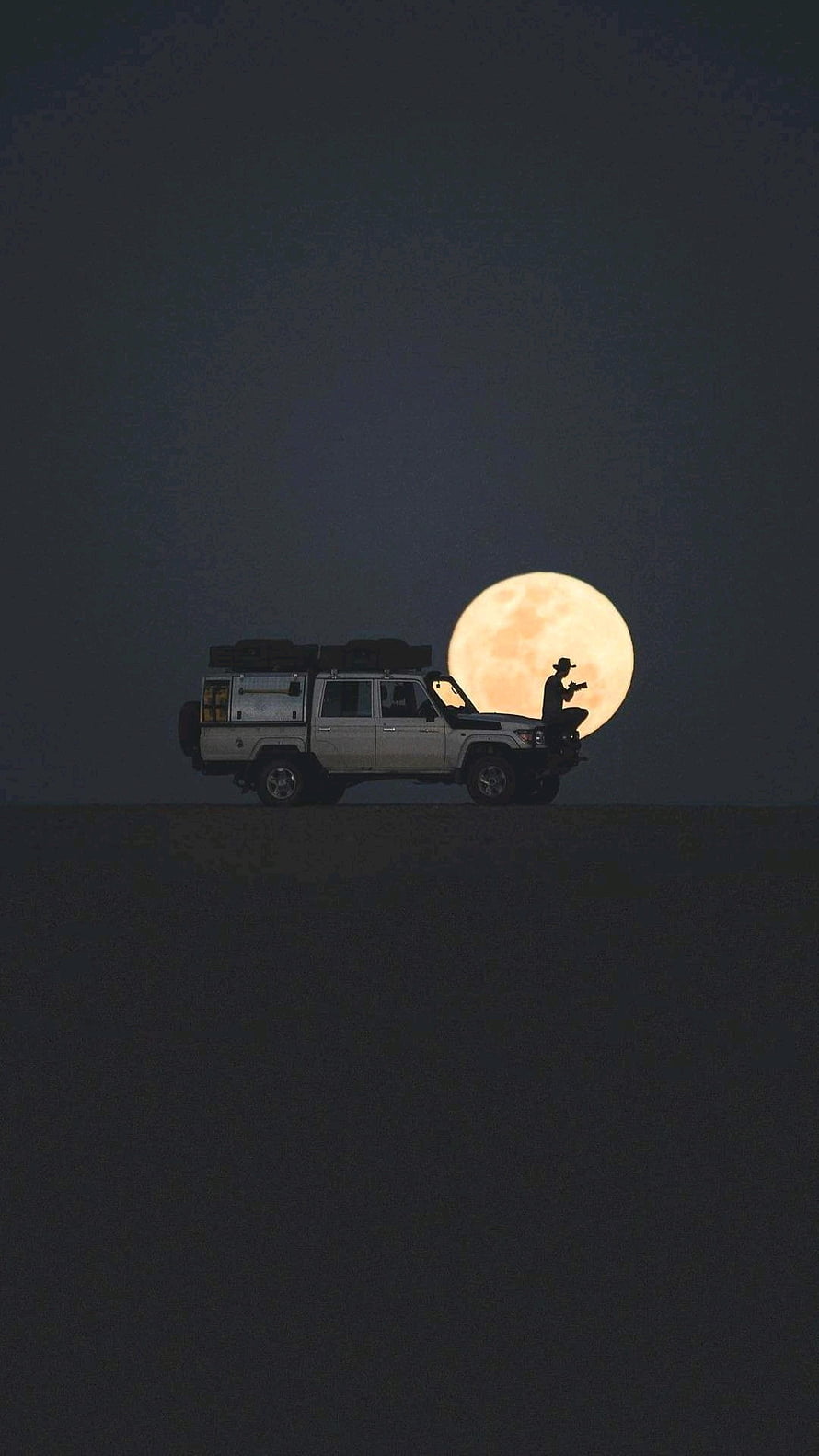 Silhouetted Off-Road Truck and Man Against a Giant Full Moon in a Dark Desert Landscape HD phone wallpaper