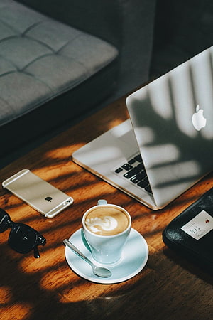 Apple MacBook and iPhone on wooden desk with cappuccino latte art and sunglasses in warm sunlight HD phone wallpaper