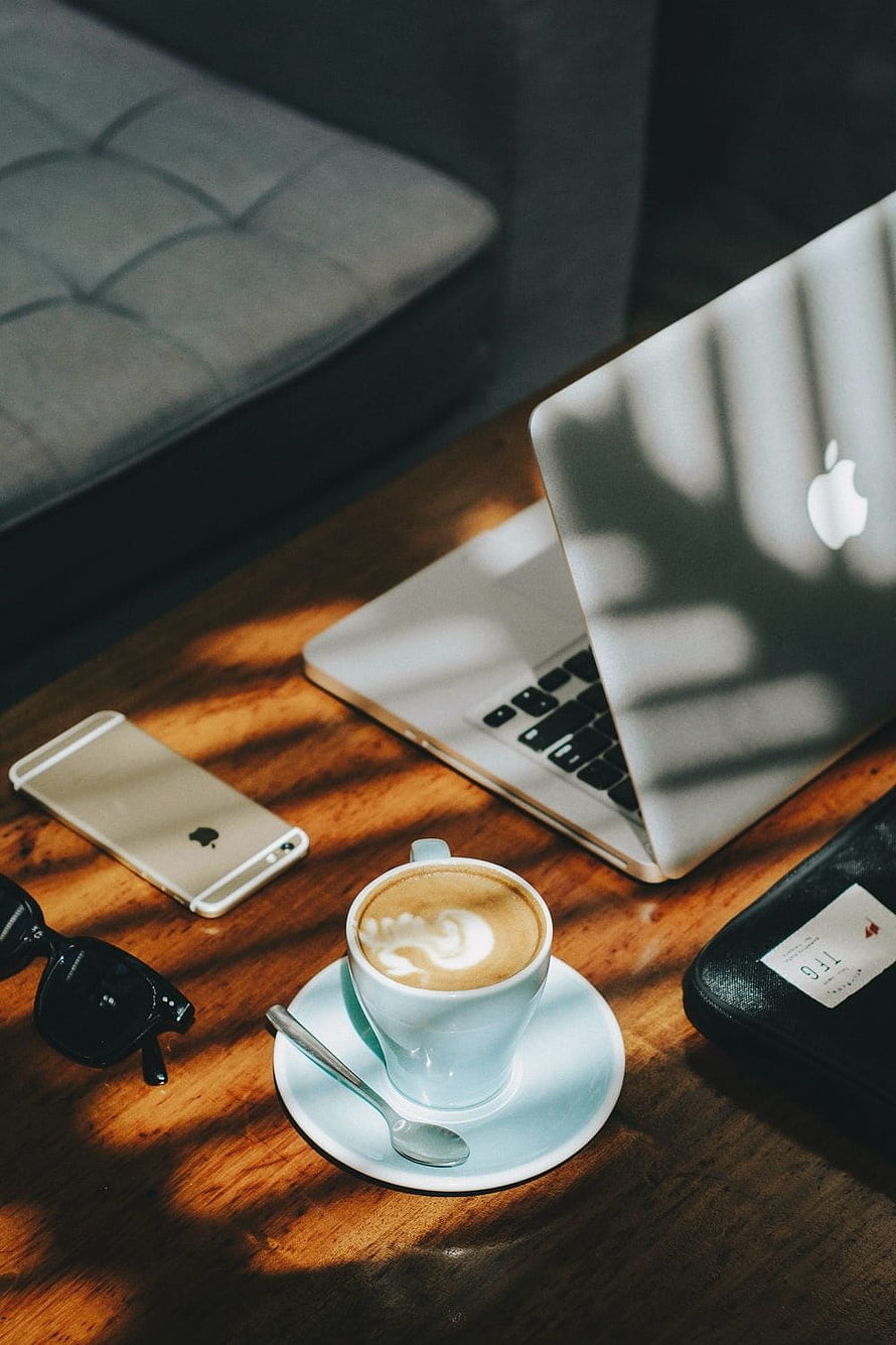 Apple MacBook and iPhone on wooden desk with cappuccino latte art and sunglasses in warm sunlight HD phone wallpaper
