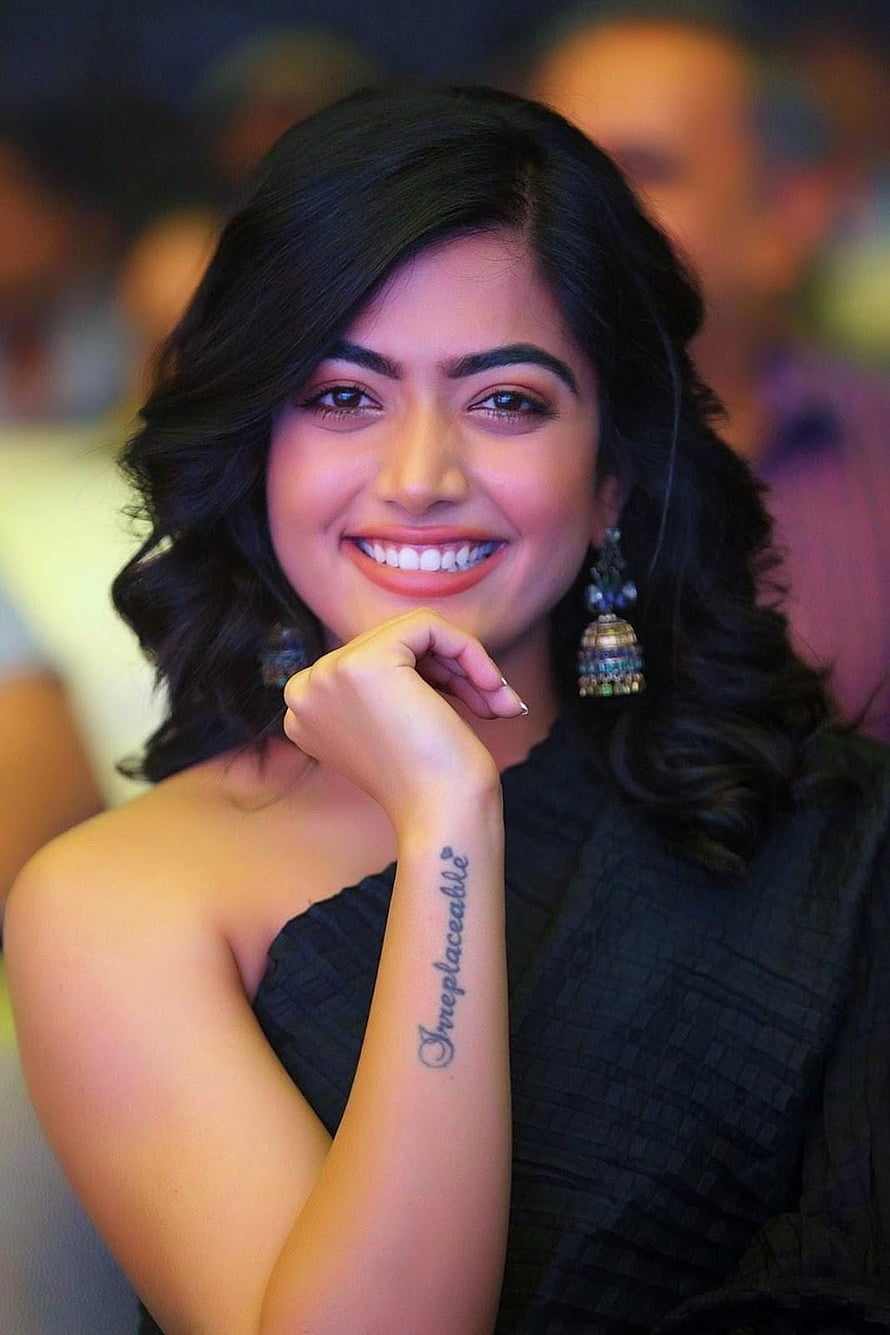 Rashmika Mandanna smiling portrait in black dress with wrist tattoo and traditional earrings HD phone wallpaper