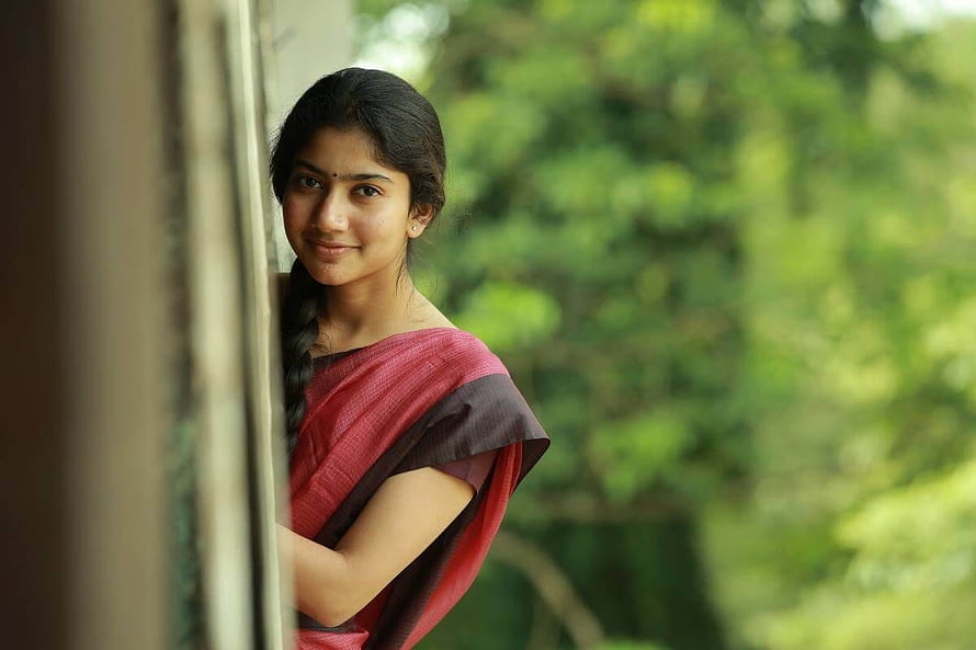 Sai Pallavi in a red sari standing by a window with a lush green garden background HD wallpaper