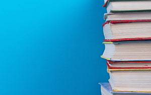 Stack of colorful hardcover books on a vibrant blue background for education and learning HD wallpaper