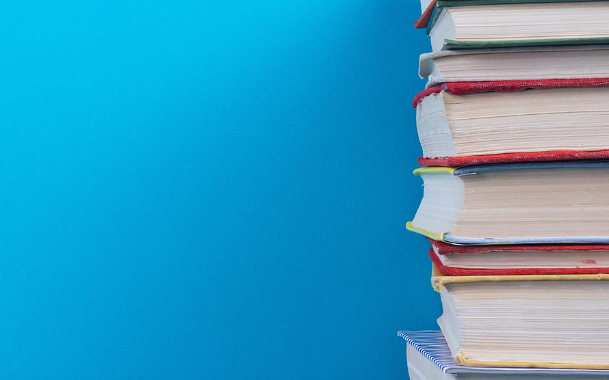 Stack of colorful hardcover books on a vibrant blue background for education and learning HD wallpaper