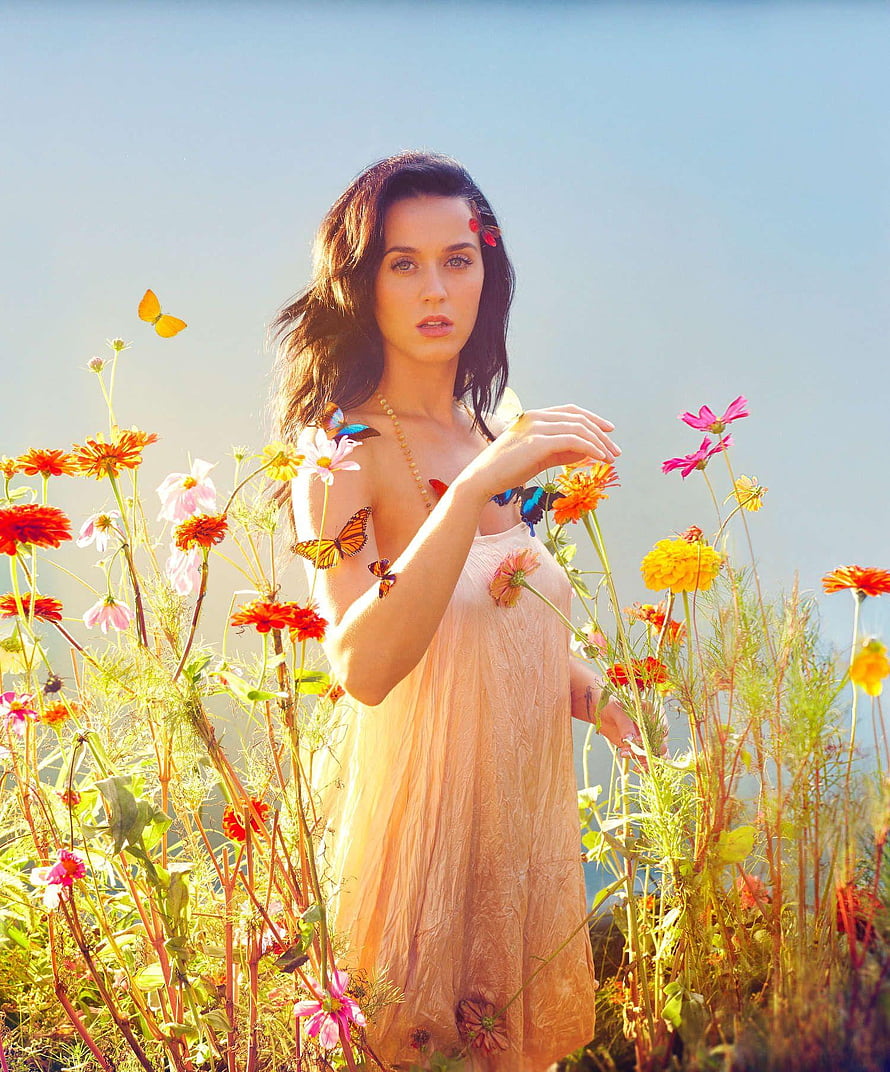 Katy Perry in a flowing peach dress surrounded by wildflowers and butterflies in a sunlit field HD phone wallpaper