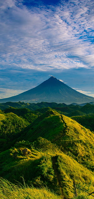 Majestic Volcanic Peak Rising Above Lush Green Rolling Hills Under a Cloudy Sky HD phone wallpaper