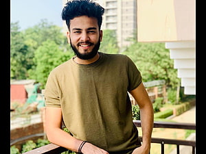 Elvish Yadav smiling portrait on a balcony with green foliage and urban buildings in the background HD wallpaper