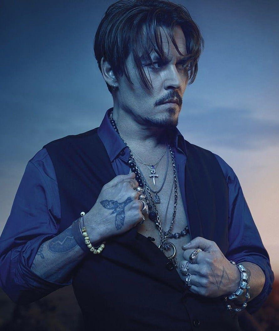 Johnny Depp in dark vest and layered chains with visible hand tattoos against a moody blue sky HD phone wallpaper