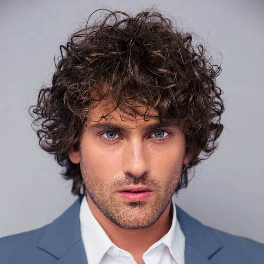 Close-up portrait of a man with voluminous dark curly hair and blue eyes wearing a grey suit jacket HD phone wallpaper