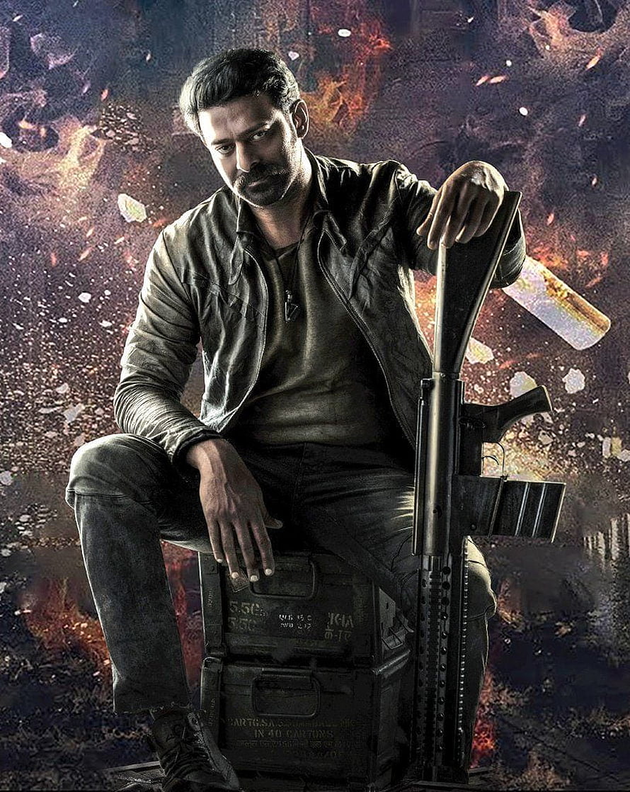 Prabhas as Salaar in gritty action pose with rifle and ammo crate HD phone wallpaper